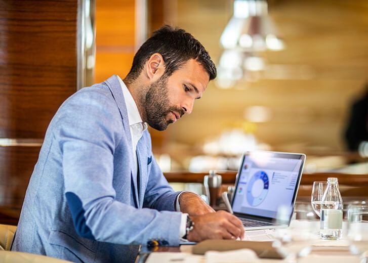 Small business owner filling a document on a clipboard while working in a restaurant. A laptop, glasses, an agenda and a water bottle are on the table.