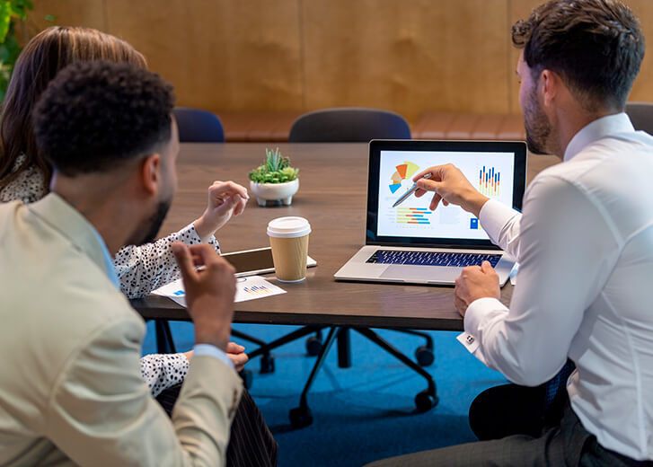 Financial advisor or lawyer with couple explaining options. They are discussing finance charts and graphs on a laptop computer. They sitting in an office and are discussing something with the agent