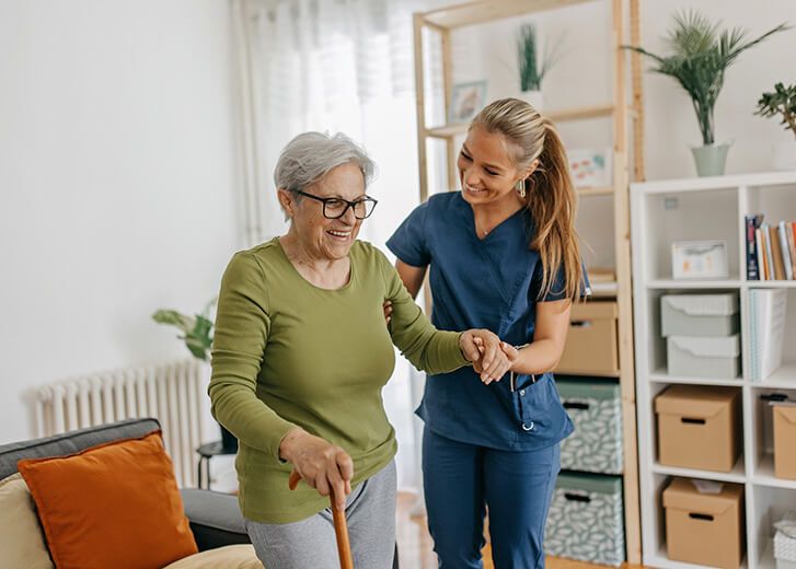 Female caregiver helping and supporting senior patient to walk at home, senior women is standing and holding walking cane