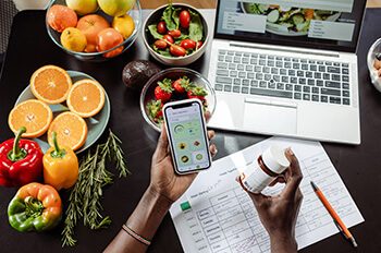 High-angle view of a woman's hands holding a smart phone and vitamin pill bottle. An unrecognizable woman is checking the nutrition facts and calorie intake of the meals.